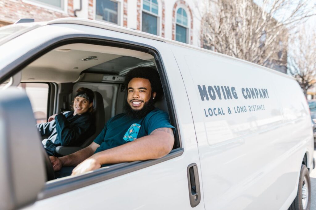 Local Beats National (If You Do It Right) Two movers smiling from their moving company van parked on a sunny day.
